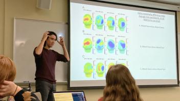 researcher gestures towards his own head while explaining a visual slide