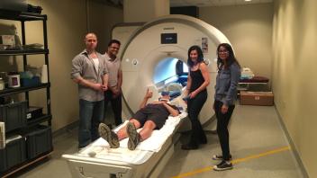 Trainees stand around an MRI machine while one lies on MRI bed